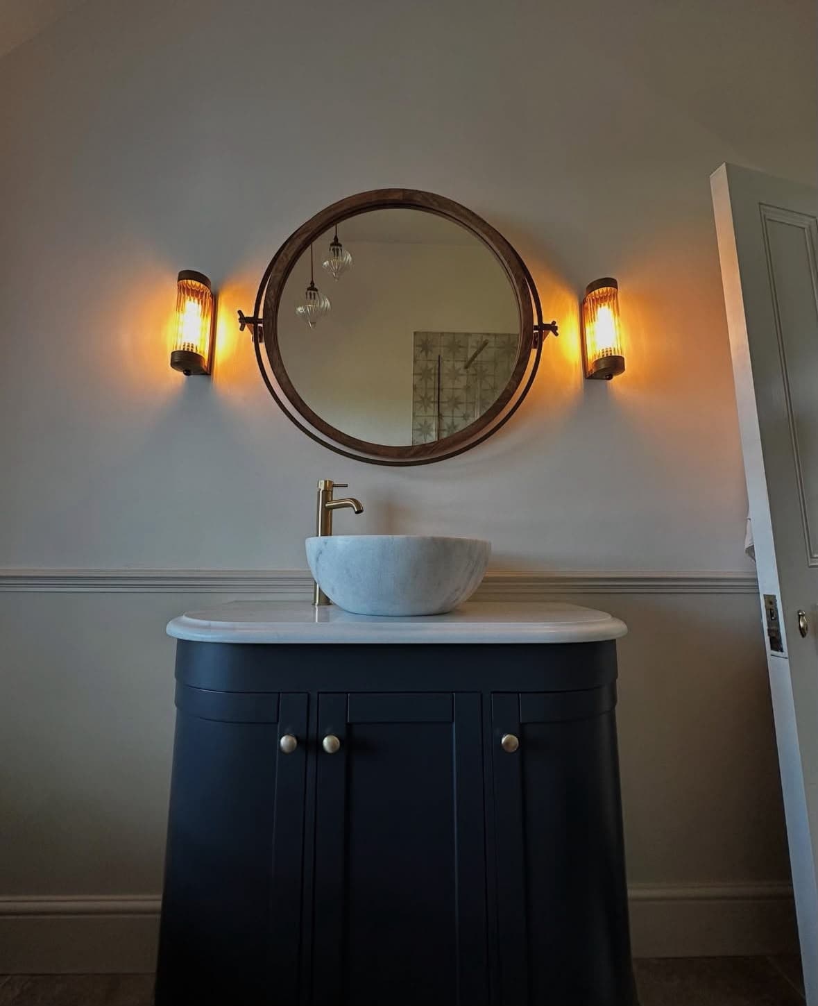 Dark navy vanity with Carrara marble vessel sink and warm wall sconces