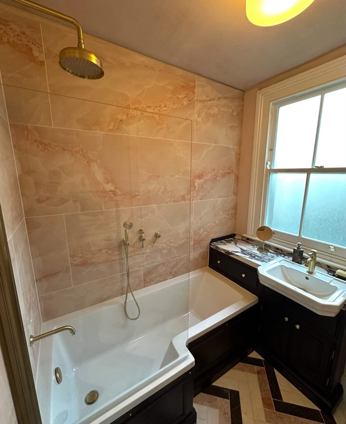 Rose marble bathroom with brass rain shower and dark vanity unit